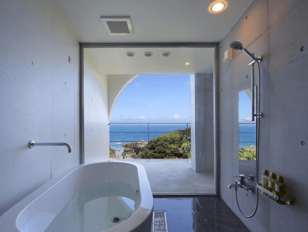 【屋久島住宿】「屋久島海洋與森林飯店（THE HOTEL YAKUSHIMA ocean & forest）附景觀浴室，大片玻璃窗直面海景與岩岸，設有浴缸與淋浴設備，是放鬆身心的療癒空間。」