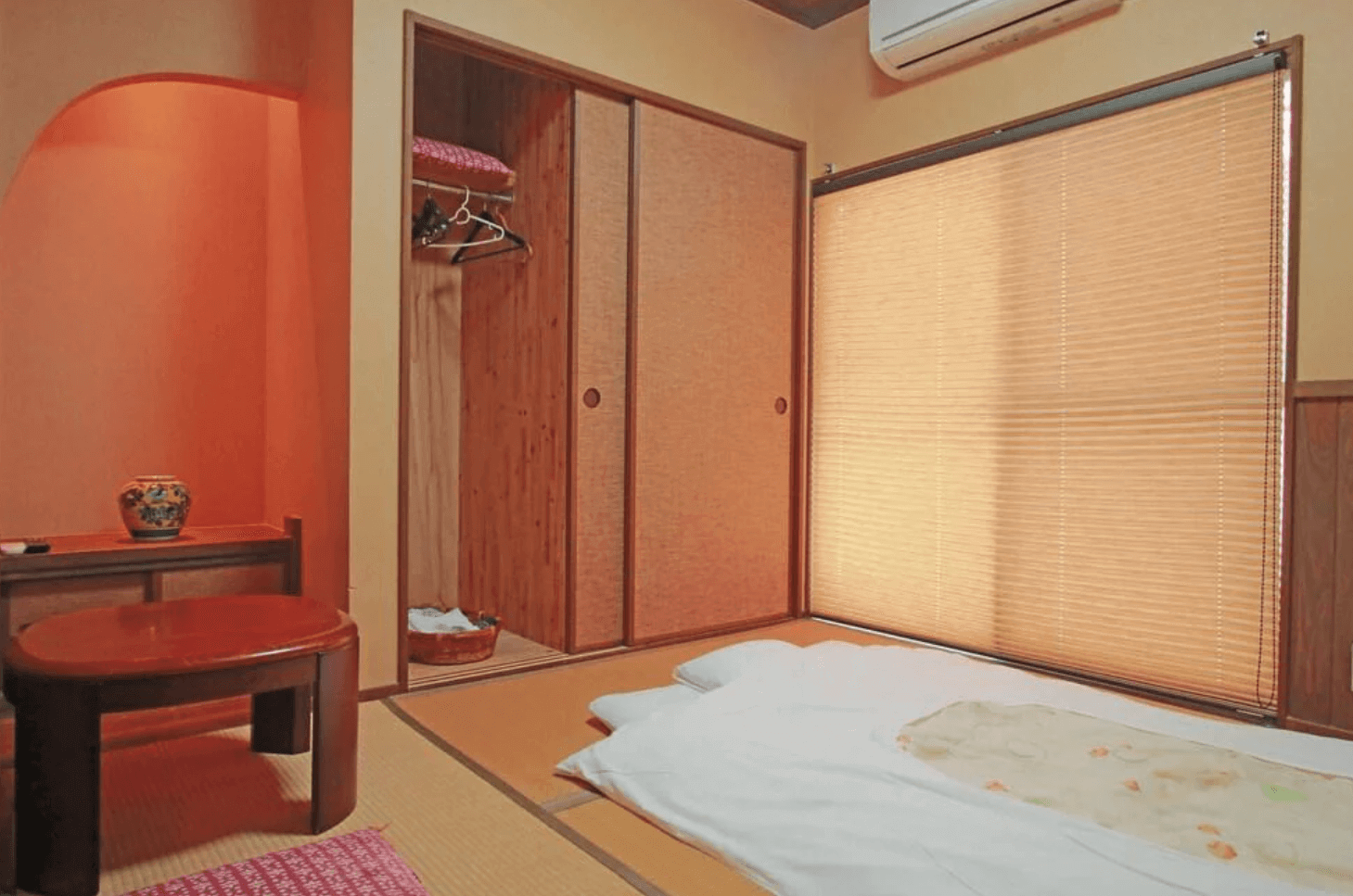 【指宿住宿】川久家庭旅館 (Family Ryokan Kawakyu) 的溫馨和室客房，鋪設舒適的日式床墊與榻榻米，房內設有小型紅色圓桌與木質衣櫃，展現傳統民宿的居家親切感。