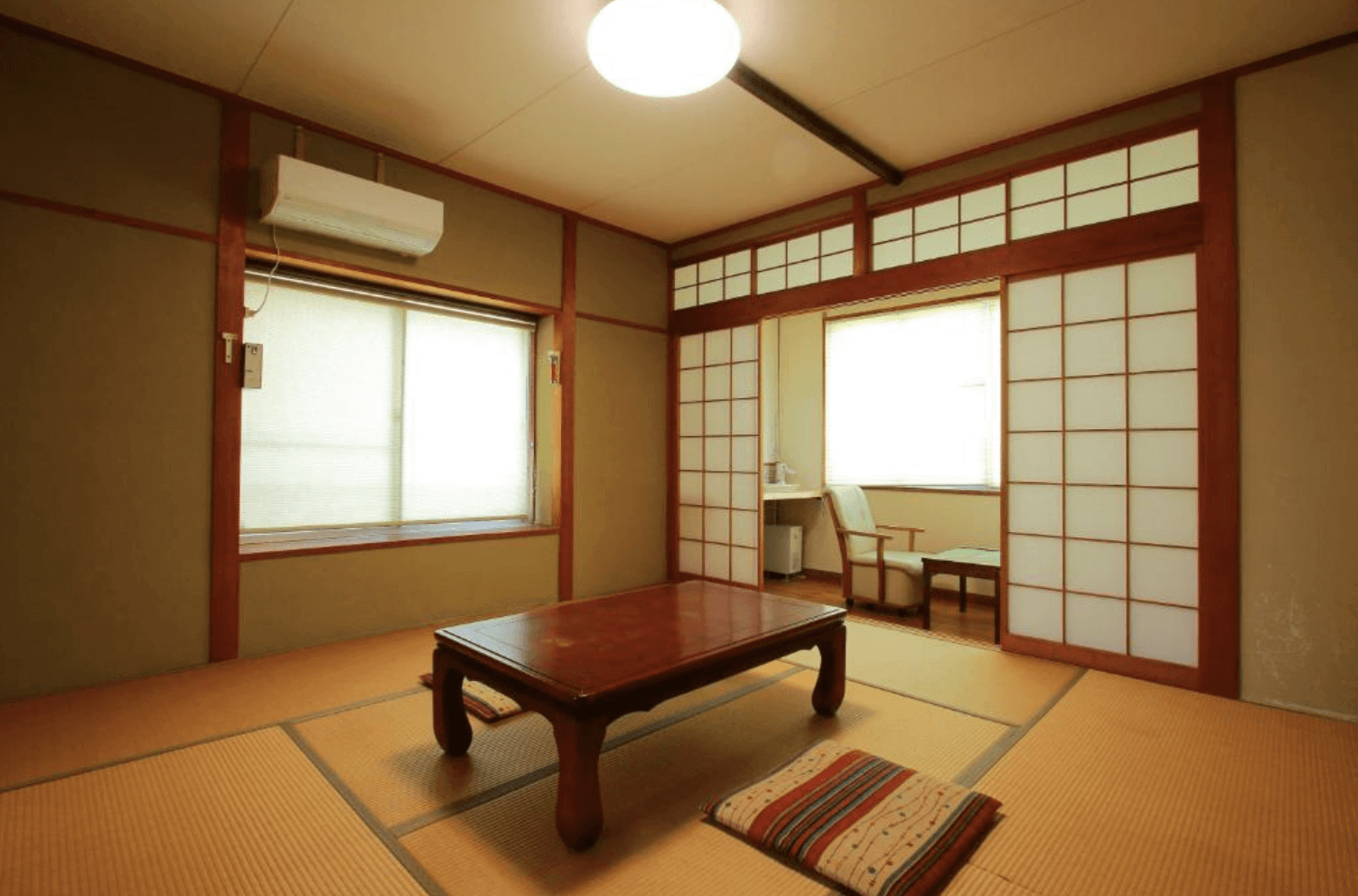 【指宿住宿】川久家庭旅館 (Family Ryokan Kawakyu) 的寬敞日式客房，中央擺放著大型木桌，透過紙拉門可通往設有觀景窗的緣側空間，提供旅客如家一般的自在休憩環境。