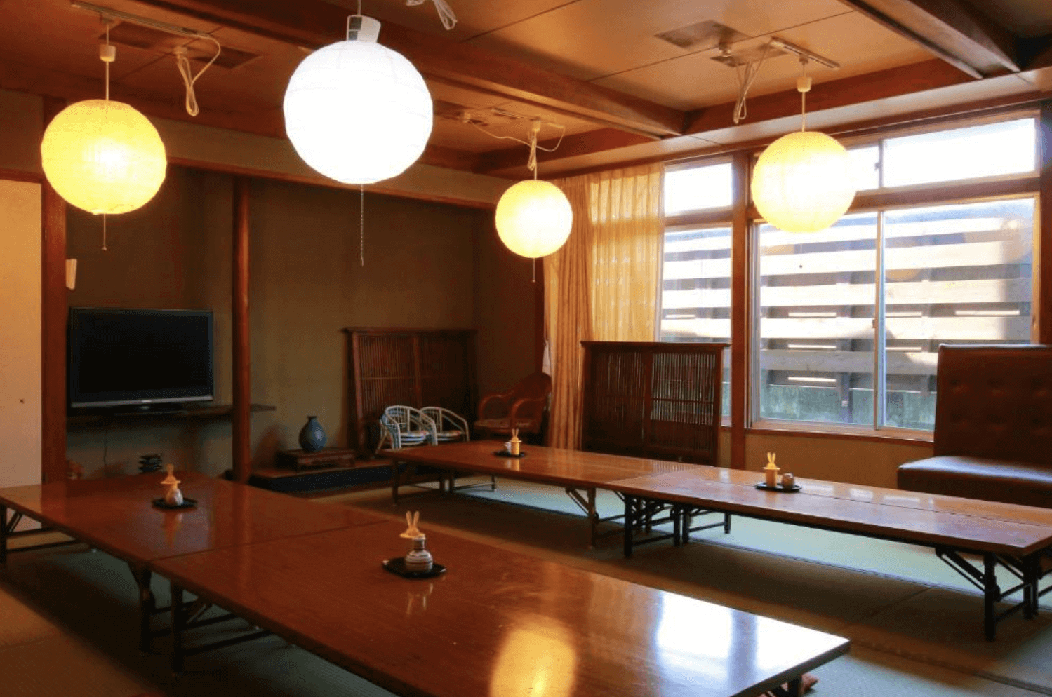 【指宿住宿】川久家庭旅館 (Family Ryokan Kawakyu) 的大廣間用餐休憩區，天花板懸掛著柔和的圓形紙燈籠，排列整齊的長桌適合團體旅客一同用餐或交流，充滿濃厚的日式懷舊風情。