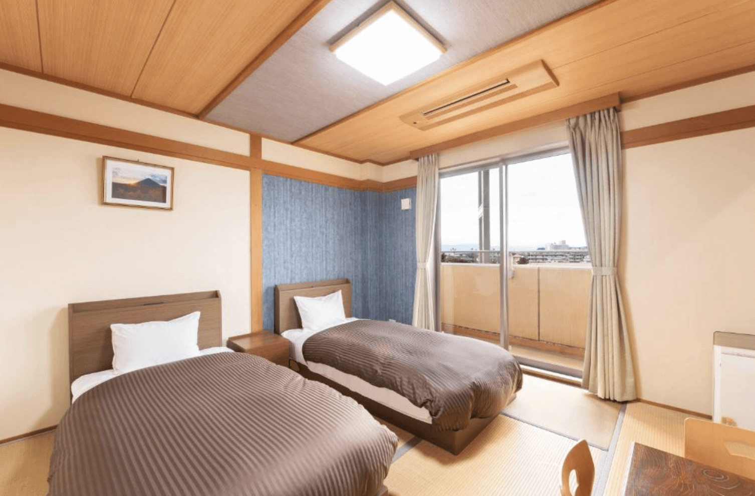 【指宿住宿】指宿Kokoro之宿 (Hotel Ibusuki Kokoronoyado) 的舒適雙床客房，結合了西式床鋪與日式榻榻米地板，房內採光良好，設有私人陽台，牆上掛著風景畫作，營造出溫馨的居家感。