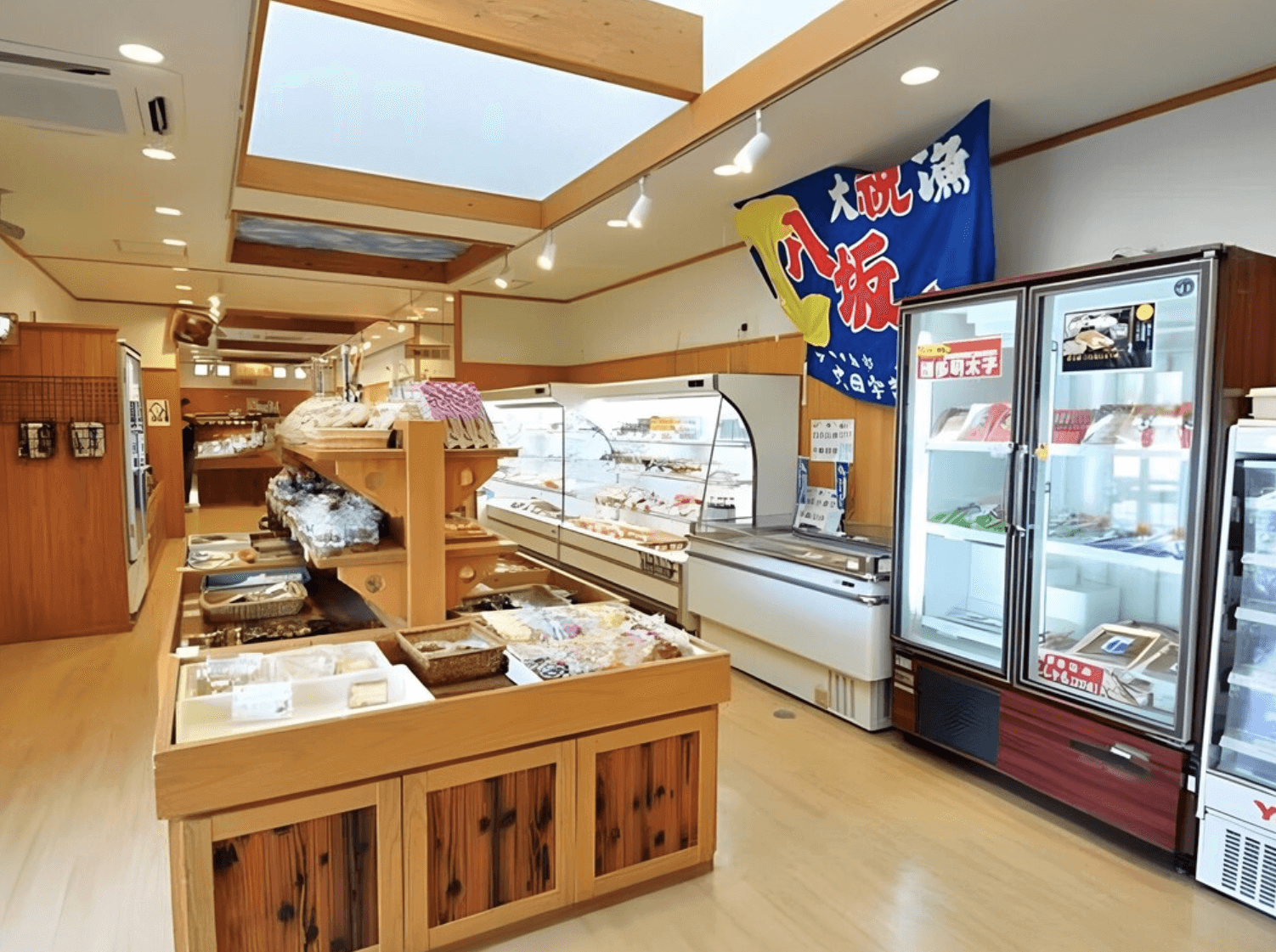 【指宿住宿】指宿Kokoro之宿 (Hotel Ibusuki Kokoronoyado) 的館內商店區，懸掛著象徵豐收的大漁旗，冷藏櫃與木製貨架上陳列著豐富的當地特產與伴手禮，方便旅客選購指宿名產。