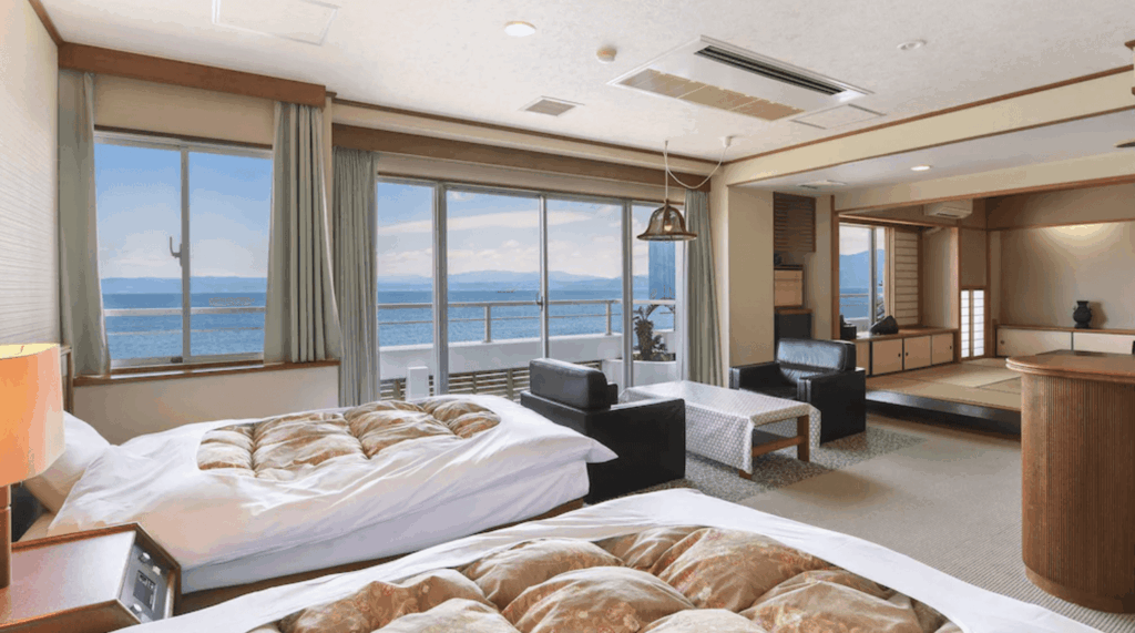 【指宿住宿】"指宿住宿精選示意圖"指宿海上飯店 (Ibusuki Kaijyo Hotel) 的海景和洋式客房，房內結合了舒適的西式雙床與日式榻榻米起居空間，落地窗外連接著觀景陽台，讓旅客在房內即可飽覽錦江灣的蔚藍海景。
