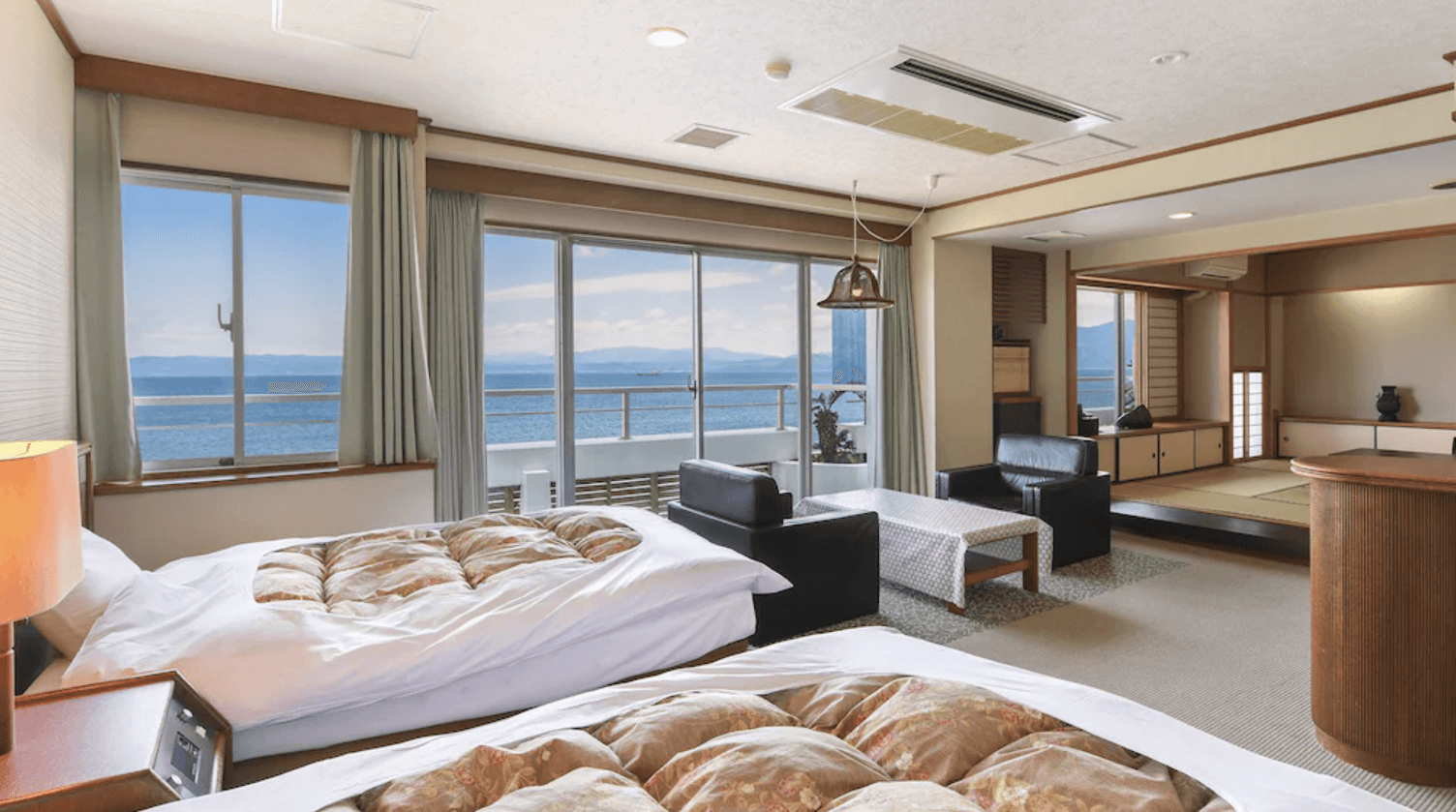 【指宿住宿】指宿海上飯店 (Ibusuki Kaijyo Hotel) 的海景和洋式客房，房內結合了舒適的西式雙床與日式榻榻米起居空間，落地窗外連接著觀景陽台，讓旅客在房內即可飽覽錦江灣的蔚藍海景。