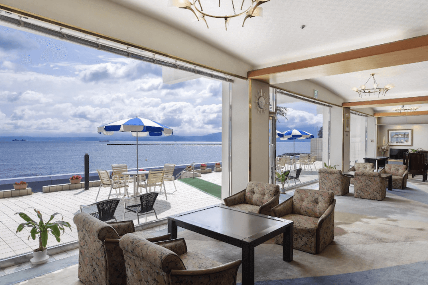 【指宿住宿】指宿海上飯店 (Ibusuki Kaijyo Hotel) 的大廳休息區與戶外露台，室內擺設復古舒適的沙發，戶外平台則設有遮陽傘座席，營造出濃厚的海岸度假氛圍。
