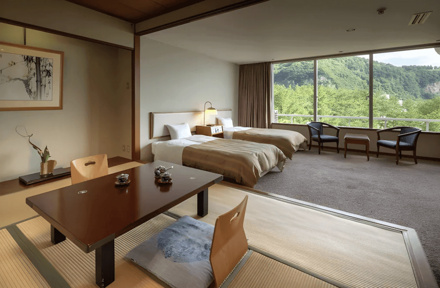 【指宿住宿】指宿白水館 (Ibusuki Hakusuikan) 的和洋式客房，前景為設有日式座桌的榻榻米休憩區，後方配置兩張舒適單人床，窗外綠意盎然的庭園山景盡收眼底，融合了傳統與現代的舒適感。