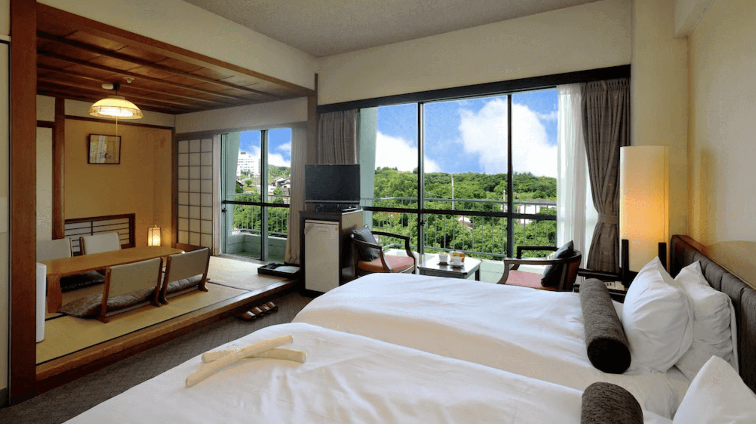 【指宿住宿】指宿皇家飯店 (Ibusuki Royal Hotel) 的標準和洋式客房，房內巧妙結合了西式雙床與架高的日式榻榻米起居區，落地窗外正對著蔥鬱的綠林與藍天景致，環境清幽舒適。