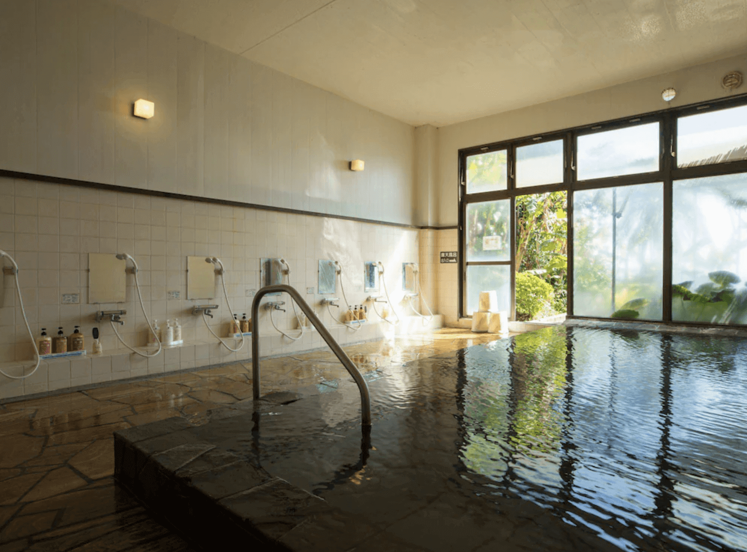 【指宿住宿】指宿皇家飯店 (Ibusuki Royal Hotel) 的大浴場，擁有寬敞明亮的空間感與整面景觀玻璃窗，旅客可在充滿開放感的環境中，邊泡湯邊欣賞戶外的綠意庭園。
