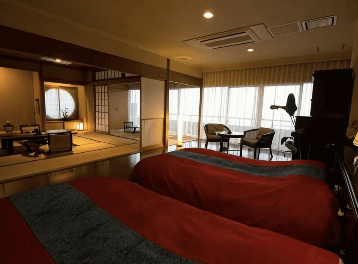 【指宿住宿】指宿秀水園旅館 (Ryokan Ibusuki Syusuien) 的和洋式客房，巧妙結合了鋪有紅色床尾巾的西式雙床與寬敞的日式榻榻米起居空間，既保有傳統風情又不失現代住宿的舒適感。