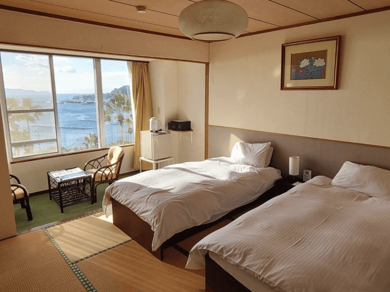 【指宿住宿】指宿鳳凰飯店 (Ibusuki Phoenix Hotel) 的和洋式度假客房，巧妙結合了榻榻米空間與西式床鋪，透過落地窗可欣賞窗外搖曳的棕櫚樹與蔚藍大海，洋溢著濃厚的南國度假氛圍。