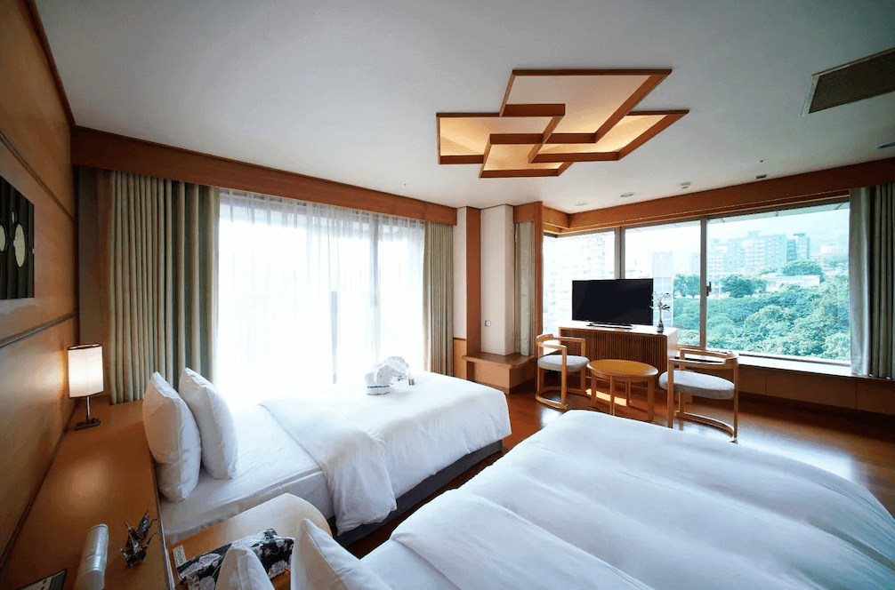 日勝生加賀屋 (Radium Kagaya) 的西式景觀客房，設計承襲日式典雅風格，配置兩張舒適單人床與窗邊休憩區，透過大面玻璃窗可飽覽北投公園的綠意與市景。