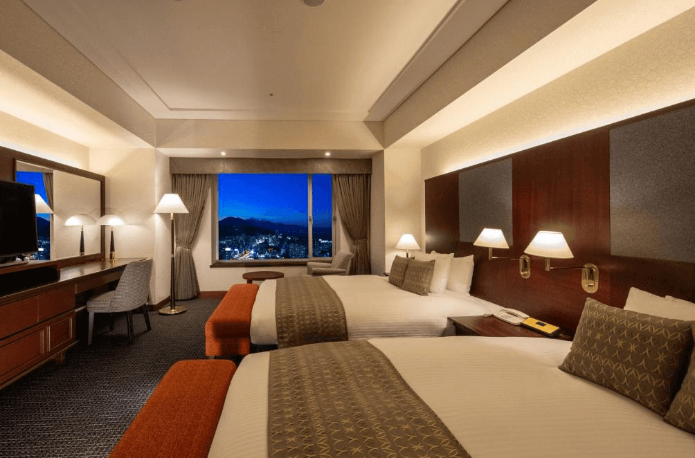 【大分住宿】日航大分綠洲塔酒店 (Hotel Nikko Oita Oasis Tower) 的景觀客房,以溫暖的木質調與橘紅色系裝飾營造舒適氛圍,最大特色是夜間透過落地窗可欣賞大分市璀璨迷人的百萬夜景,展現身為當地最高地標的優勢。