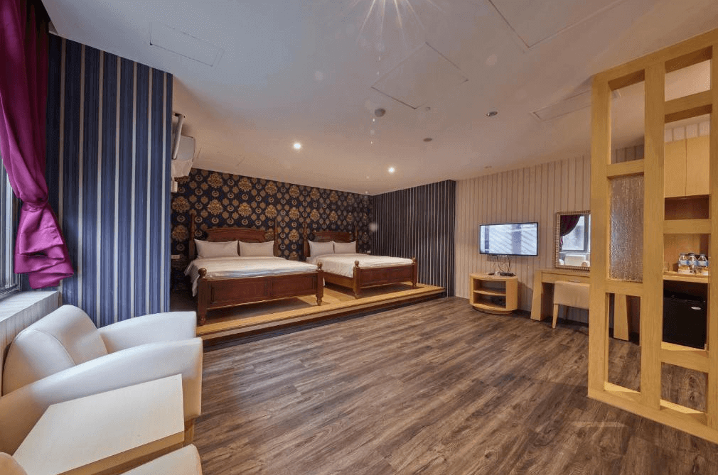 曲水會館 (Grand Villa) 的豪華四人客房，裝潢充滿濃厚的歐式宮廷風情，採用深色花紋壁紙搭配典雅的木質雙人大床，房內設有精緻的白色沙發休憩區與梳妝台，營造出高貴的住宿氛圍。