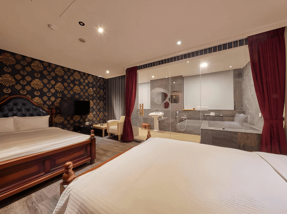 曲水會館 (Grand Villa) 的客房視角，透過大面透明玻璃隔間可看見衛浴空間，房內配備深色木質大床與華麗的歐式床頭板，搭配紫紅色的厚重窗簾，展現獨特的復古奢華感。