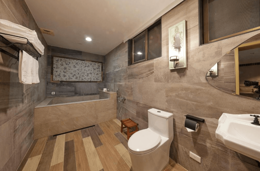 曲水會館 (Grand Villa) 的衛浴空間，牆面鋪設帶有紋理的暖色系磁磚，設有寬敞的石造泡澡浴池與復古風格的壁燈，提供旅客在私密空間中享受放鬆的沐浴時光。