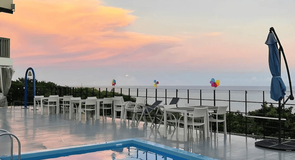 【沖繩南城住宿】榮耀島沖繩藪宿度假村 (Glory island okinawa Yabusachi Resort) 的戶外泳池區，夕陽時分天空被染成夢幻的粉紫色，池畔設有戶外用餐座席，是欣賞沖繩南部絕美日落的理想地點。