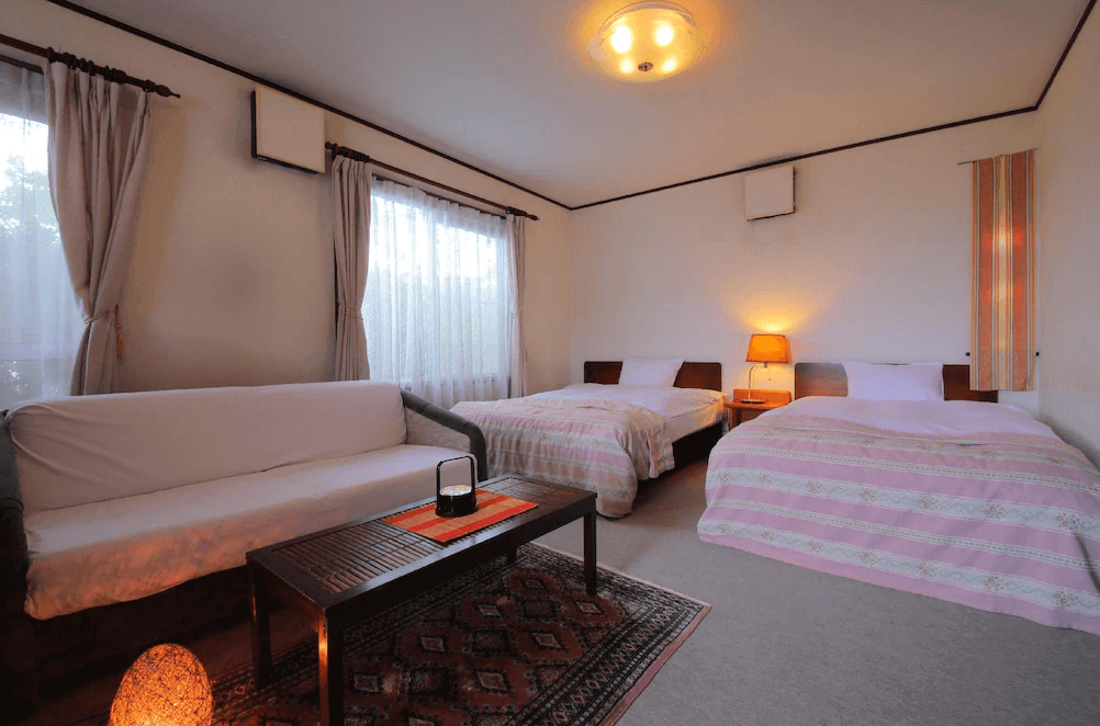 【霧島住宿】櫻櫻溫泉旅館的西式客房，空間寬敞，配置兩張單人床以及一區帶有沙發與木茶几的客廳休息區，風格溫馨典雅。