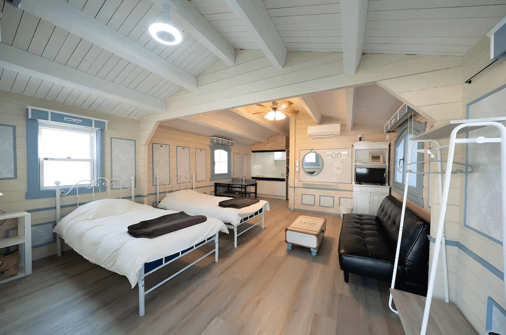 【屋久島住宿】「莫瑞諾考卡吉小屋（Cottage Morinokokage）寬敞明亮的雙床房，挑高木質天花與鄉村風格裝潢，設有沙發與簡易廚房，營造溫馨舒適的度假小屋氛圍。」