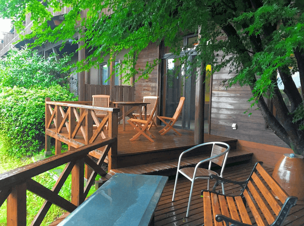 【霧島住宿】霧島溫泉旅人山莊飯店，被翠綠楓葉與樹木環繞的戶外木製露台休息區，設有休閒桌椅供旅客放鬆享受自然氛圍。