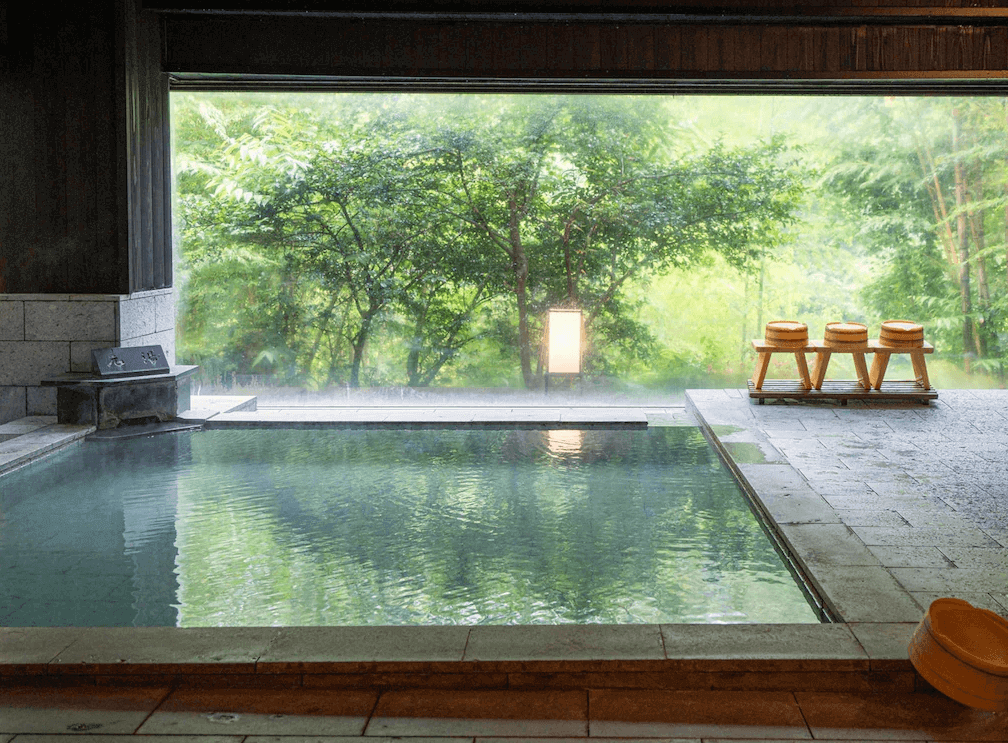 【霧島住宿】霧島紅葉谷清流莊的室內溫泉浴池，擁有一整面巨大的觀景窗，將窗外翠綠的楓葉與森林美景如畫般引入室內，提供絕佳的視覺享受。