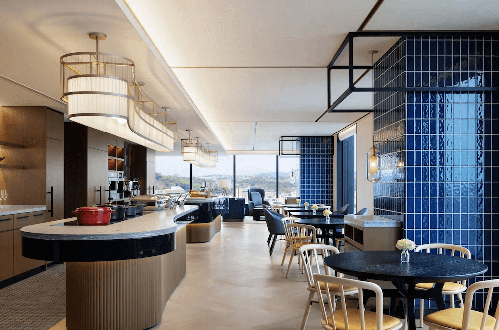 【鹿兒島住宿】鹿兒島喜來登 (Sheraton Kagoshima) 的現代風格餐飲空間，設有醒目的深藍色磁磚裝飾柱與流線型造型吊燈，明亮的取餐檯與舒適的木質桌椅區，營造出優雅的用餐氛圍。