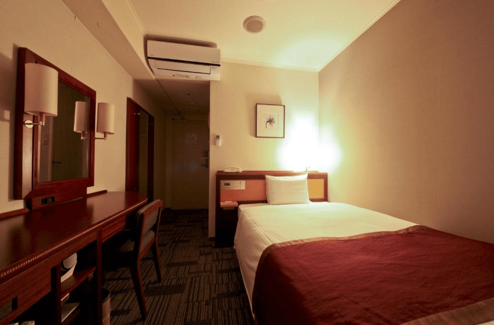 【鹿兒島住宿】鹿兒島法華俱樂部飯店 (Hotel Hokke Club Kagoshima) 的標準單人客房，空間配置精巧實用，設有寬敞的木質長桌與梳妝鏡，搭配鋪有紅色床尾巾的舒適單人床，非常適合商務旅客入住。