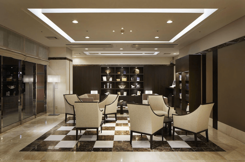 【鹿兒島住宿】鹿兒島法華俱樂部飯店 (Hotel Hokke Club Kagoshima) 的大廳休憩區，地面鋪設經典的黑白格紋大理石，搭配米色系高背沙發椅與沉穩的深色展示櫃，營造出寧靜優雅的迎賓氛圍。