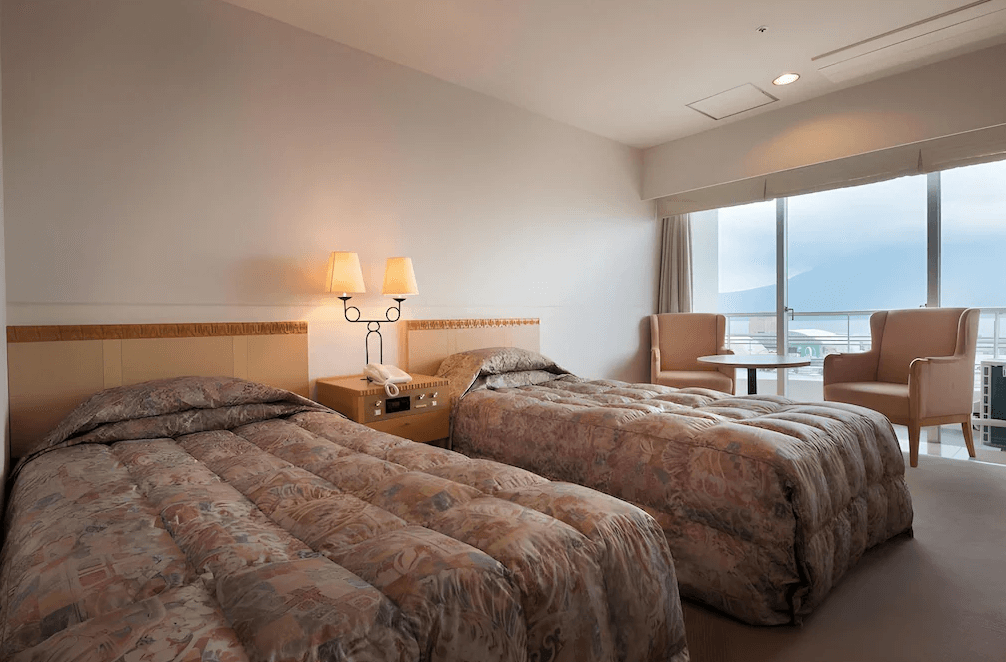 【鹿兒島住宿】鹿兒島陽光皇家飯店 (Kagoshima Sun Royal Hotel) 的標準雙床客房，兩張單人床鋪設典雅花紋床單，房內設有觀景陽台與休憩桌椅，提供旅客欣賞海灣景色的私人空間。