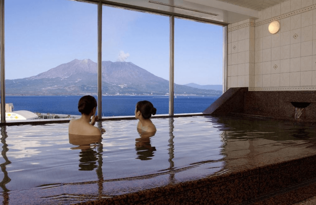 【鹿兒島住宿】鹿兒島陽光皇家飯店 (Kagoshima Sun Royal Hotel) 的展望溫泉大浴場，擁有整面寬闊的玻璃景觀窗，旅客可浸泡在寬敞浴池中，毫無遮蔽地眺望櫻島火山與碧藍海景。
