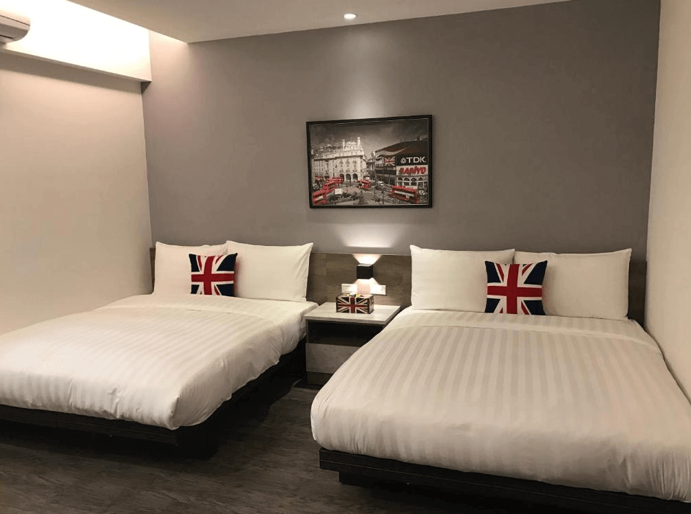 177旅行公寓英倫風雙床房，灰藍色牆面掛有倫敦街景黑白畫作，床上點綴著英國國旗圖案抱枕，營造出簡約時尚的異國住宿氛圍。