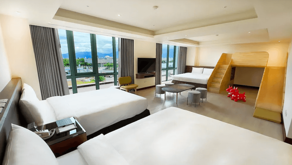 【台東寵物友善住宿】"台東寵物友善住宿精選示意圖"娜路彎大酒店 (Naruwan Hotel) 的豪華親子客房，房內最大亮點是設有專屬的木質溜滑梯雙層床與可愛的紅色Rody跳跳馬，搭配兩張寬敞舒適的雙人床與落地景觀窗，是台東極具代表性的家庭友善房型。