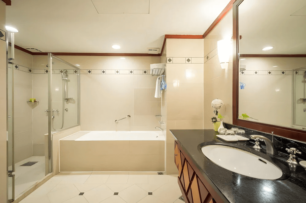 【台東寵物友善住宿】娜路彎大酒店 (Naruwan Hotel) 的客房衛浴設施，採用標準的乾濕分離設計，配有獨立的淋浴間與寬敞的泡澡浴缸，米色系石材牆面營造出潔淨明亮的盥洗空間。