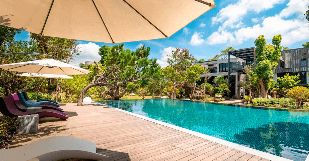 【苗栗寵物友善住宿】"苗栗寵物友善住宿精選示意圖"寨酌然野奢庄園 (The Modol) 的戶外戲水泳池區，被周圍蔥鬱的老樹與自然植被緊密環抱，池畔鋪設木棧平台並配有休閒躺椅與遮陽傘，後方可見設計感十足的現代建築，營造出隱世而獨立的度假天堂氛圍。