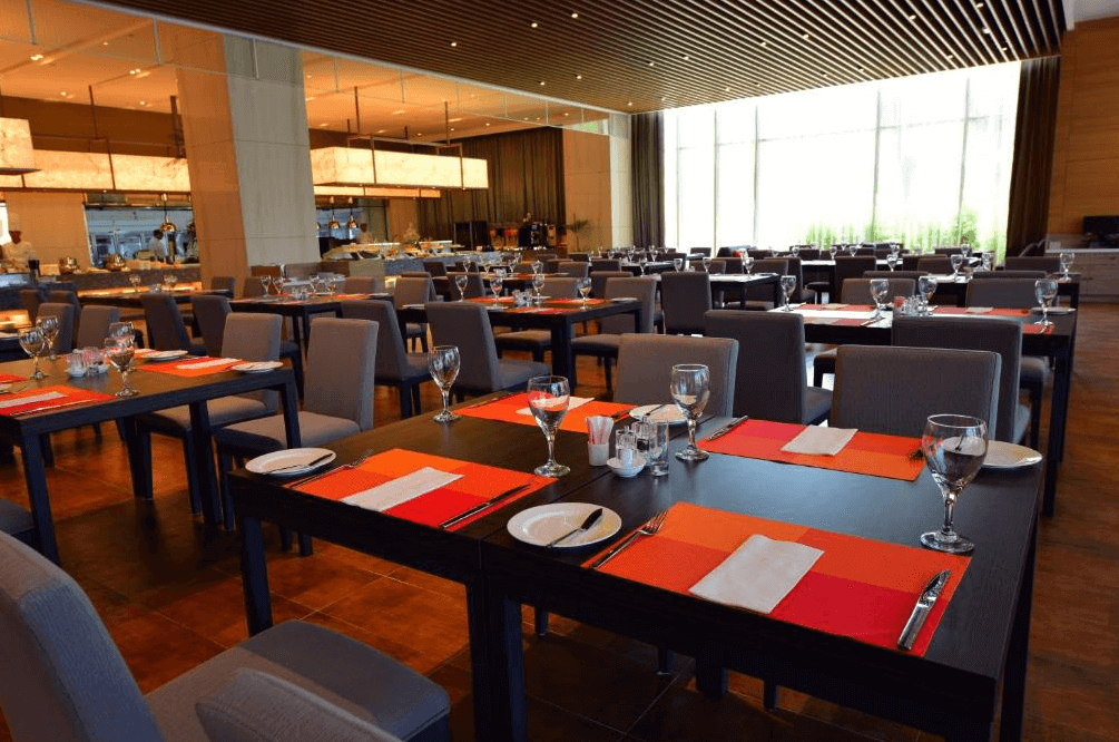 尚順君樂飯店歐式自助餐廳，挑高的用餐空間開闊氣派，整齊排列的深色餐桌搭配鮮豔的橘紅色餐墊，後方為豐富的自助取餐區，是家庭聚餐與大型宴會的理想場所。