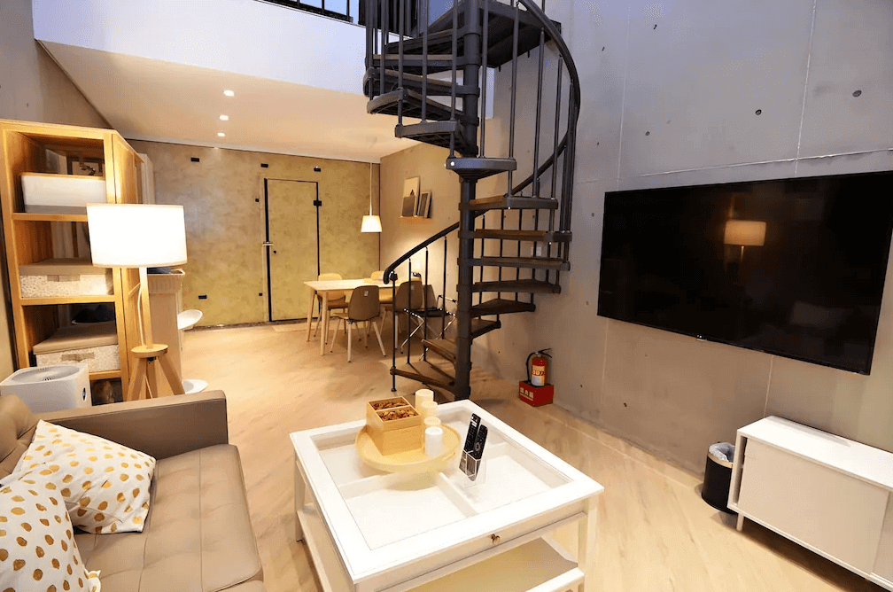 "南投市住宿精選示意圖"智旅南投體驗館Loft風客廳，挑高的清水模質感牆面搭配搶眼的黑色旋轉樓梯，配置超大尺寸壁掛電視與溫馨沙發區，是適合親友包棟聚會的寬敞起居空間。