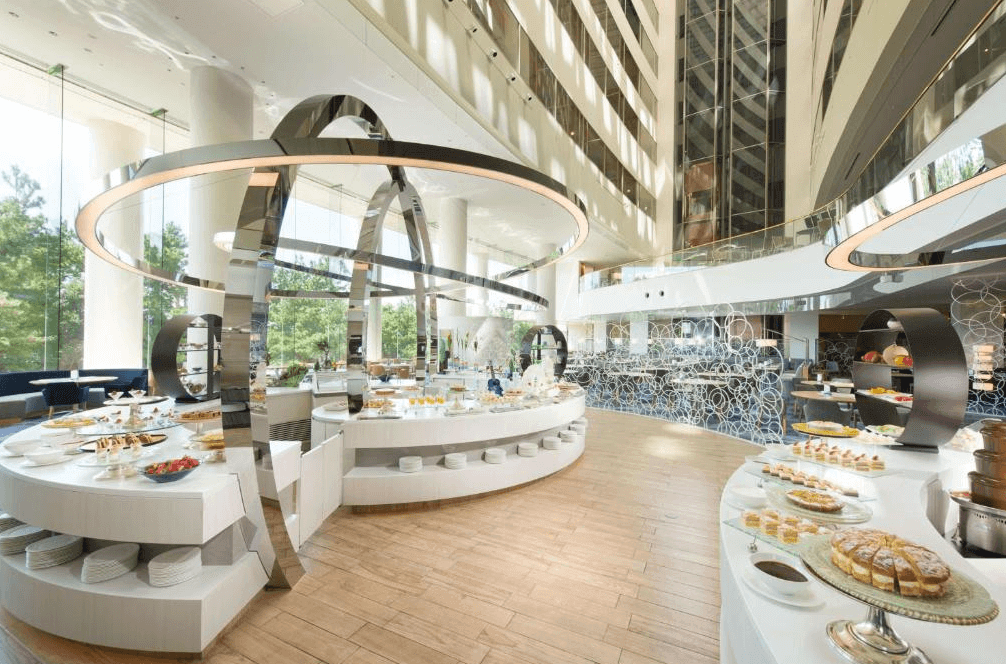 東京希爾頓酒店的挑高大廳自助餐廳,空間開闊明亮,擁有壯觀的銀色弧形裝置藝術,餐台上擺滿了各式精緻甜點與料理。