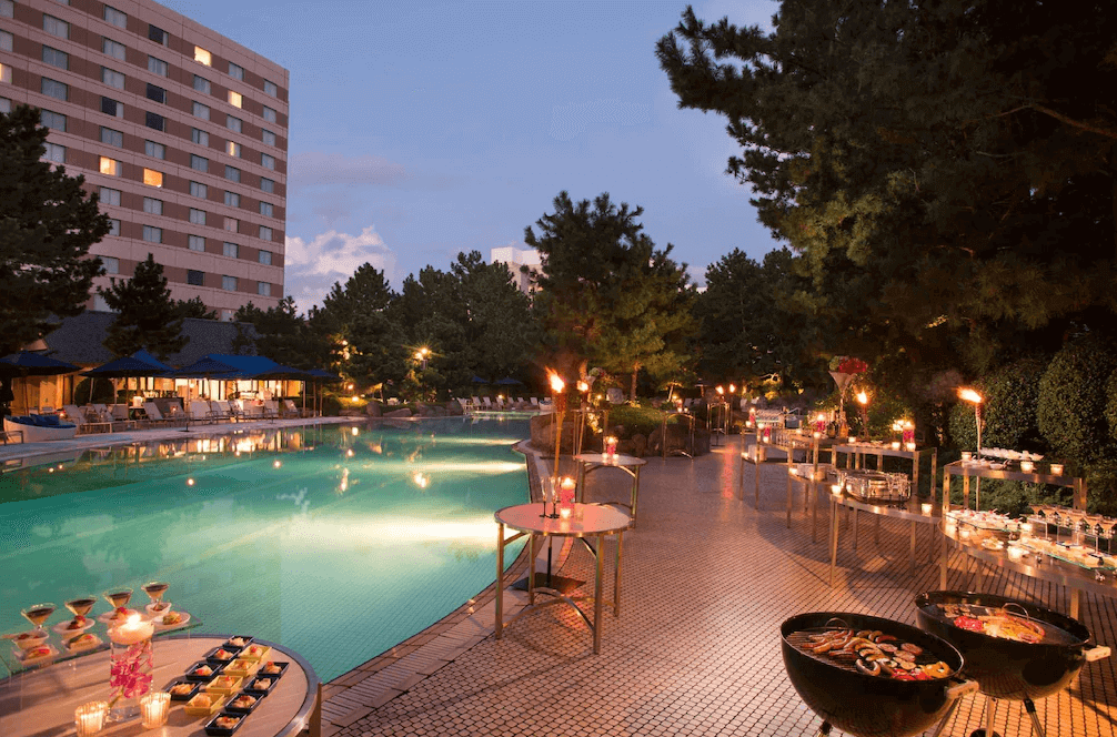 "新宿住宿精選示意圖"東京希爾頓酒店的戶外泳池畔，夜間點亮了浪漫燈火，設有池畔BBQ燒烤與自助餐區，營造出悠閒奢華的度假晚宴氛圍。