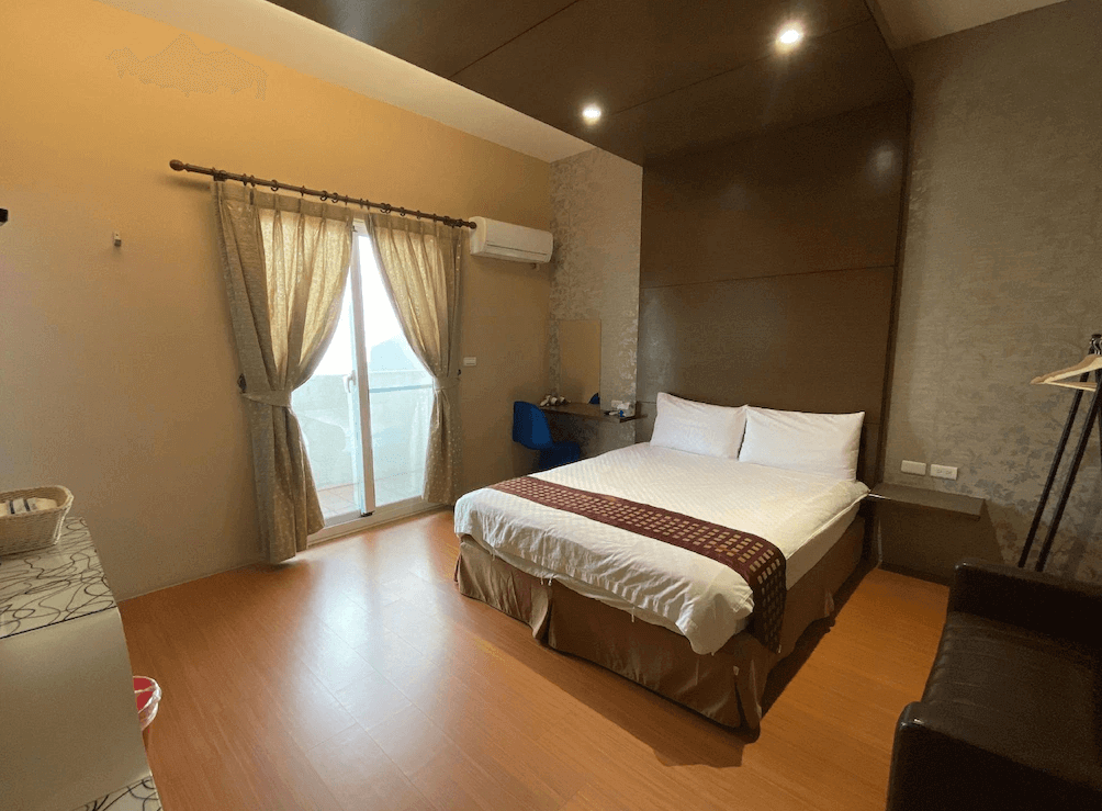 【台東寵物友善住宿】樂活小築民宿 (Lohas Homestay) 的簡約風格客房，床頭設計採用深褐色木質飾板延伸至天花板，增添空間層次感，大面落地窗外連接專屬陽台，採光良好且空間寬敞。