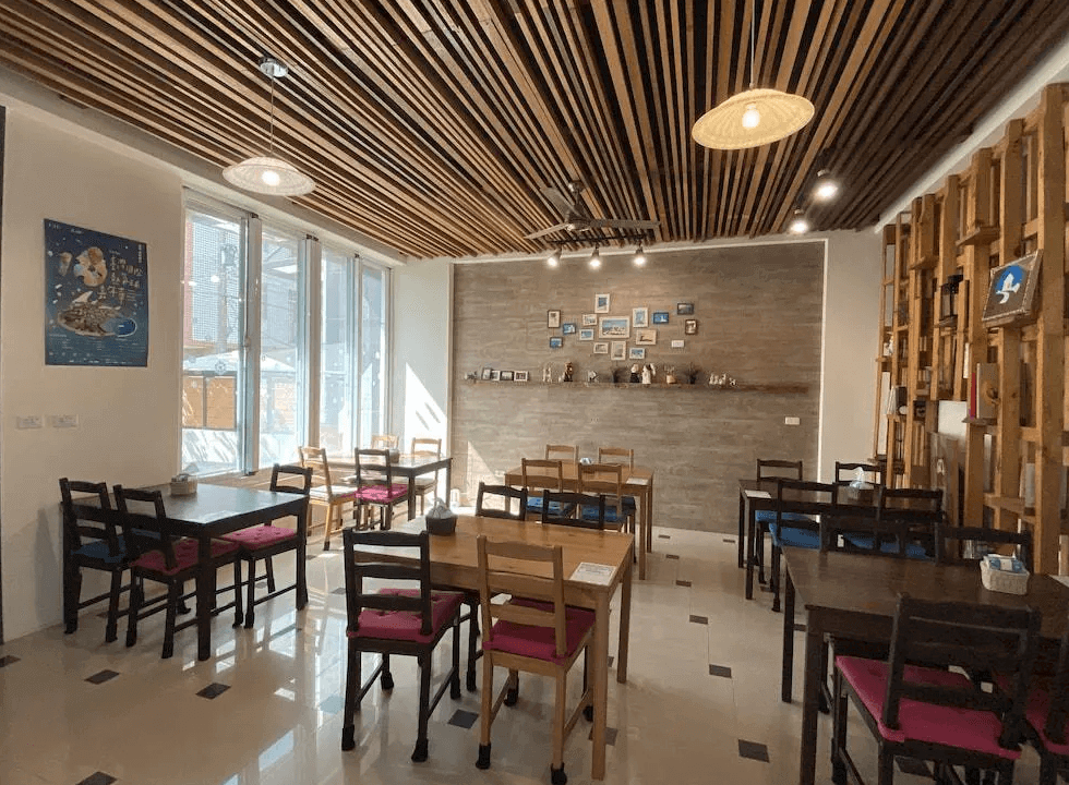【台東寵物友善住宿】樂活小築民宿 (Lohas Homestay) 的公共交誼廳與餐廳，天花板採用獨特的木格柵線條設計，搭配溫潤的木質餐桌椅與牆面相片牆裝飾，空間充滿文青質感與居家溫馨感。
