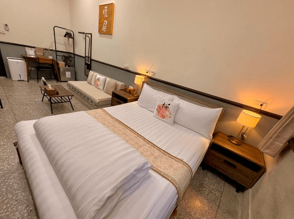 "竹南住宿精選示意圖"櫻花樹夏民宿懷舊雙人房，保留傳統的磨石子地板，搭配溫馨雙人床與日式小客廳區，牆面掛有書法裝飾，營造出濃厚的復古居家氛圍。