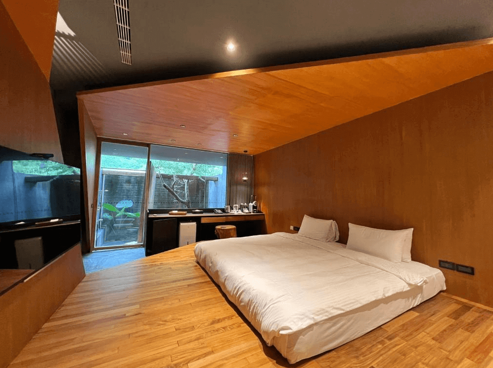 【苗栗寵物友善住宿】泰安觀止溫泉會館 (Onsen Papawaqa) 的特色客房，展現獨特的清水模建築美學，床鋪設置於不規則切角的溫潤木地板平台上，搭配斜頂天花板設計，營造出被大自然與原木包圍的穴居安全感。