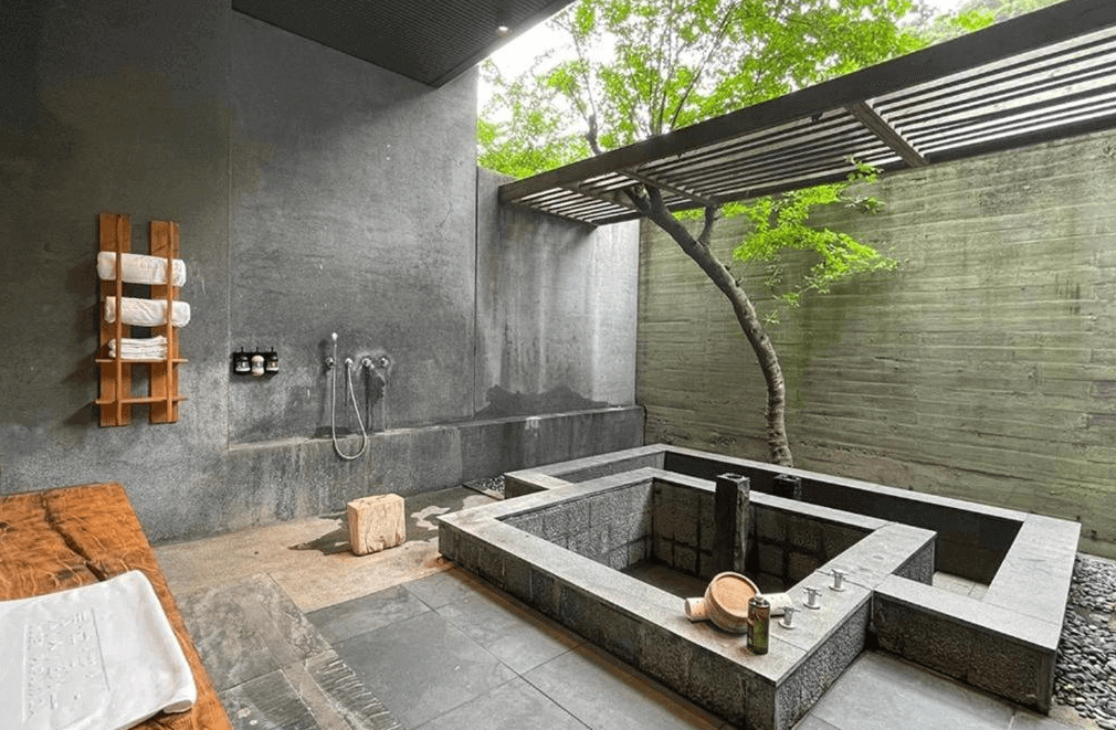 【苗栗寵物友善住宿】泰安觀止溫泉會館 (Onsen Papawaqa) 的半露天私人湯屋，以粗獷的清水模牆面搭配石造冷熱雙泉池，天井處特別保留了原生綠樹，讓旅客在光影交錯的隱密空間中，享受與自然共生的泡湯體驗。
