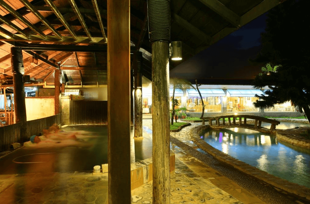 【台東寵物友善住宿】知本泓泉溫泉渡假村 (Rainbow Resort) 最著名的戶外露天溫泉區「美人湯」，夜間燈光投射在木造迴廊與招牌的拱型小橋上，營造出充滿懷舊風情的泡湯氛圍，讓旅客在森林芬多精中徹底放鬆。