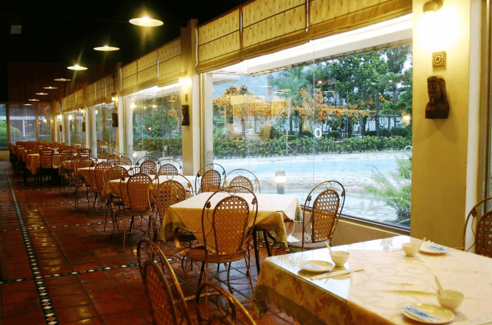【台東寵物友善住宿】知本泓泉溫泉渡假村 (Rainbow Resort) 的景觀餐廳，採用大面積的落地玻璃窗設計，將戶外翠綠的庭園植栽與泳池景色引入室內，搭配復古風的籐編餐椅，提供旅客明亮舒適的用餐環境。