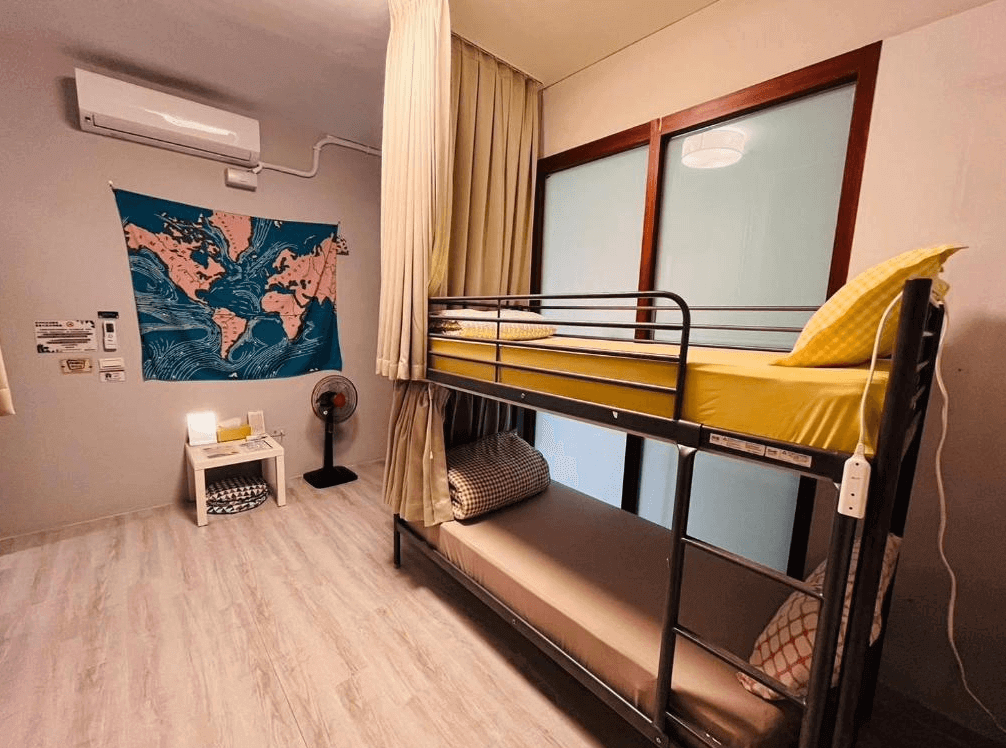綠色的日子民宿溫馨上下舖房型，牆面掛有世界地圖布幔增添旅行氛圍，配置堅固的金屬雙層床架，並擁有大面落地窗與遮光拉簾，採光良好且空間利用率高。