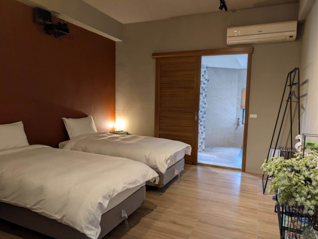 自然野奢203號房室內一景，採雙床（Two Single Beds）配置，適合朋友出遊或喜歡獨立睡眠空間的旅客，房內木質拉門與綠植擺設增添自然氣息。