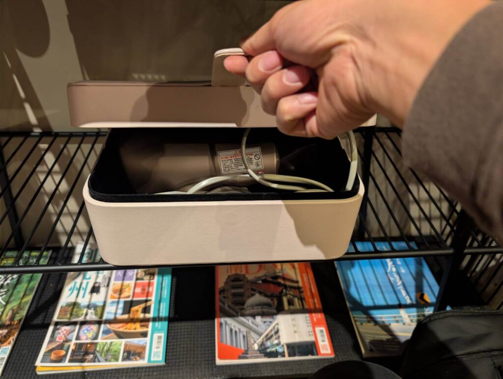 自然野奢客房的貼心備品特寫，畫面展示開啟米色質感收納盒的瞬間，內附知名品牌 Panasonic 吹風機，下方整齊陳列著旅遊雜誌，展現對住客使用體驗的重視。