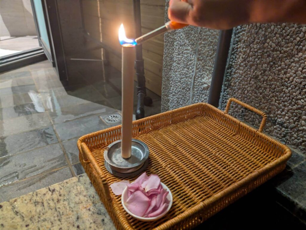 自然野奢的泡湯儀式感特寫，在戶外浴池旁點燃艾草芳香棒，藤編托盤上另備有玫瑰花瓣，增添嗅覺與視覺的雙重享受。