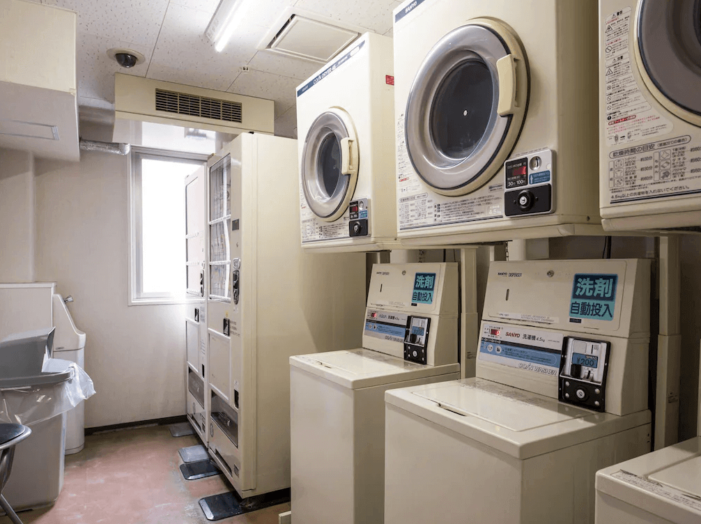 西鐵INN新宿的自助洗衣房,整齊排列著多台投幣式洗衣機與烘衣機(洗劑自動投入),並設有飲料自動販賣機,生活機能設施完善。