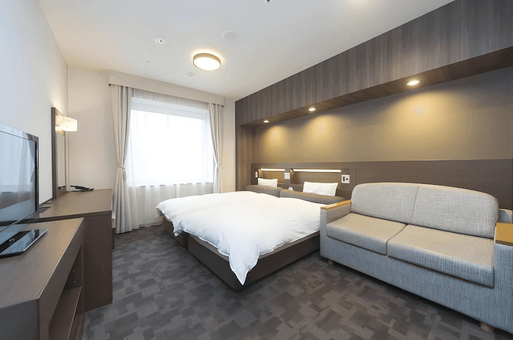 Dormy Inn澀谷神宮前溫泉舒適三人房，採用沈穩的深色木質調裝潢，配置一張雙人大床與單人床，並設有溫馨的沙發休憩區，適合小家庭或好友三人出遊入住。